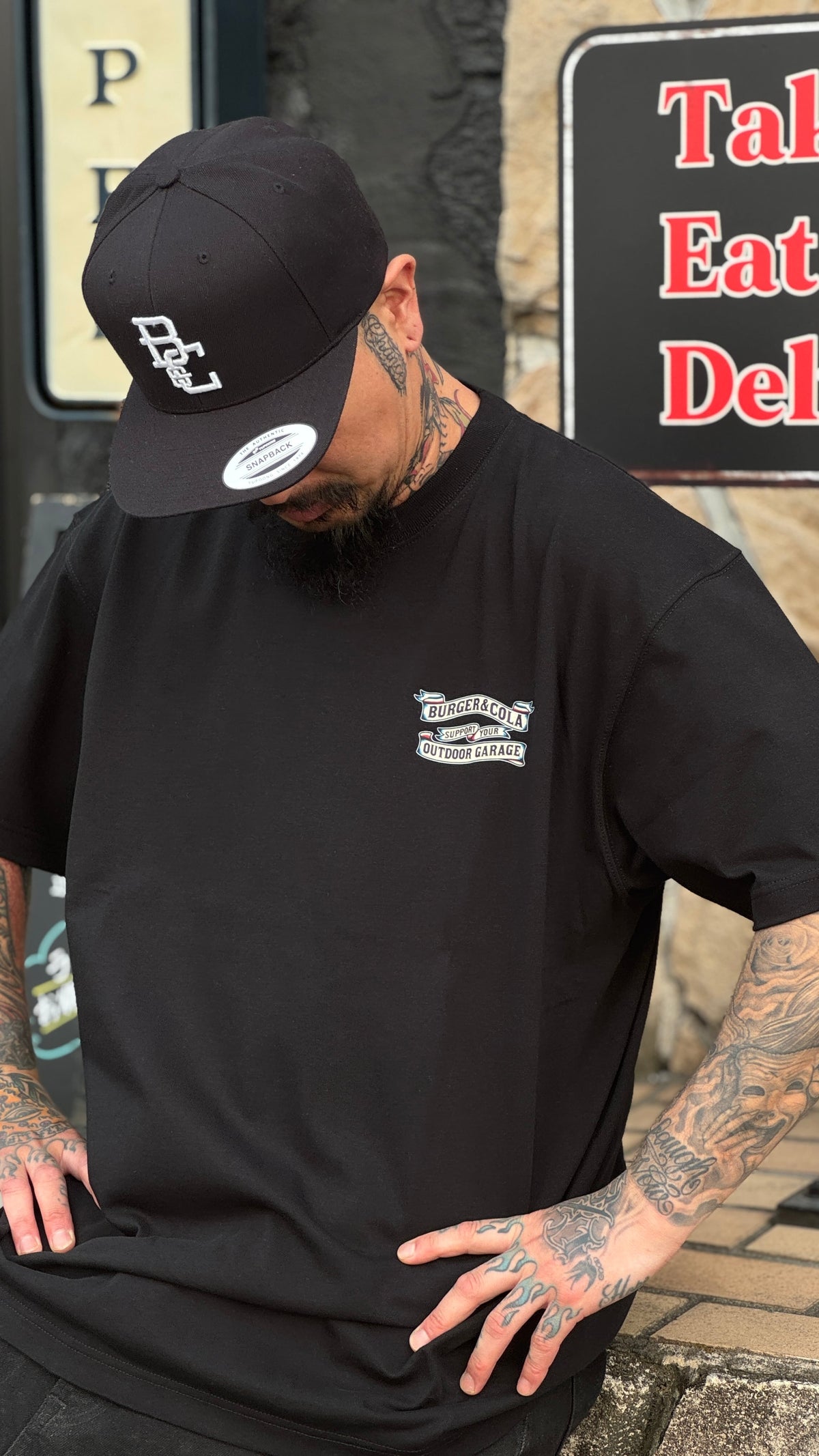 BURGER&COLA B&C BASEBALL CAP（ベースボールキャップ）黒キャップ着用イメージ、黒Tシャツと合わせて（店舗前）