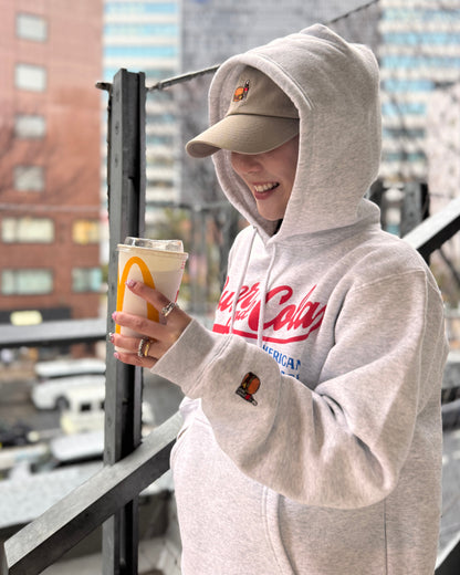 BURGER&COLA B&C LOW CAP（ローキャップ）ベージュ着用イメージ、パーカーと合わせてドリンクを持つ様子